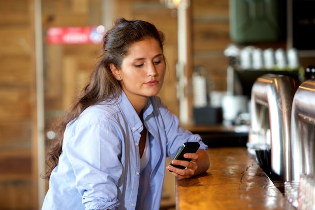 Jonge vrouw aan de bar met behulp van de mobiele telefoon