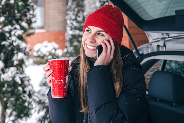 Jonge vrouw aan de telefoon die in de winter in de buurt van de auto staat