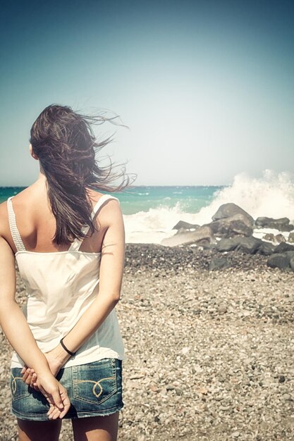 Foto jonge vrouw aan de zee van achteren met haar in de wind