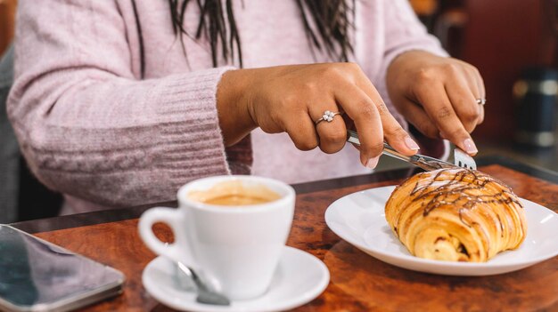 Jonge vrouw aan het ontbijt met croissant en koffie