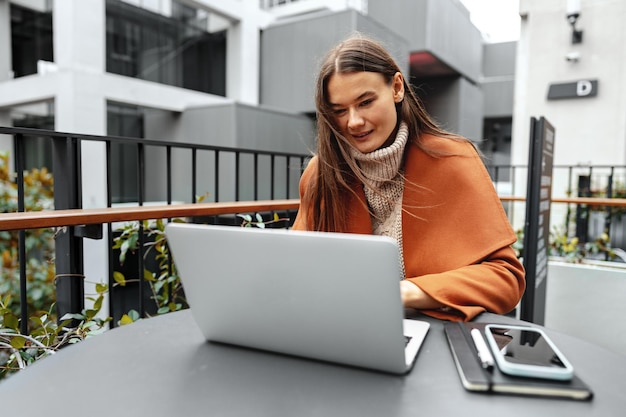 Jonge vrouw aan het werk met haar laptop zittend aan de tafel in de straat