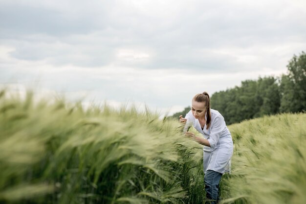 Jonge vrouw agronoom in witte jas gehurkt in groene tarweveld en gewaskwaliteit controleren.