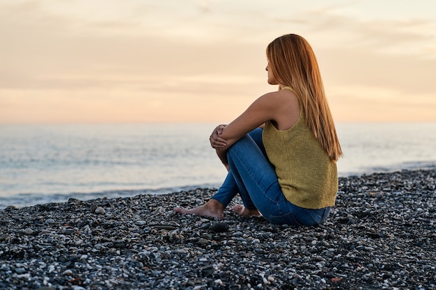 Jonge vrouw alleen zittend op strandzand bij zonsondergang. Concept van ontspanning en meditatie