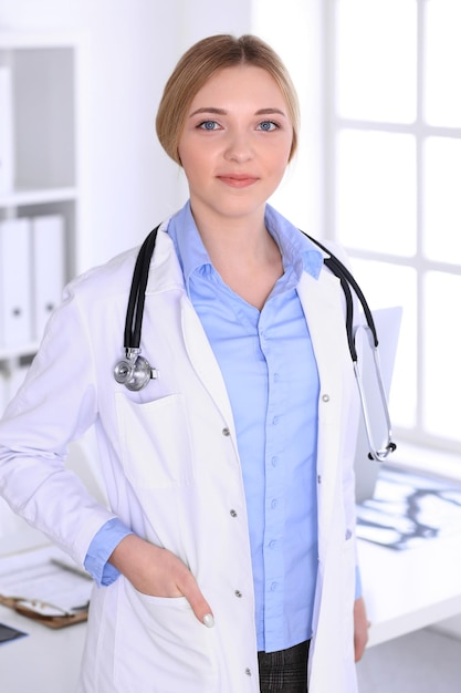 Jonge vrouw arts aan het werk in het ziekenhuis camera kijken. Kakikleurige blouse van therapeut ziet er goed uit. Geneeskunde en gezondheidszorg concept.