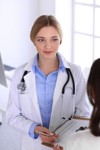 Jonge vrouw arts en patiënt bij medisch onderzoek op ziekenhuiskantoor. Blauwe kleur blouse van therapeut ziet er goed uit. Geneeskunde en gezondheidszorg concept.