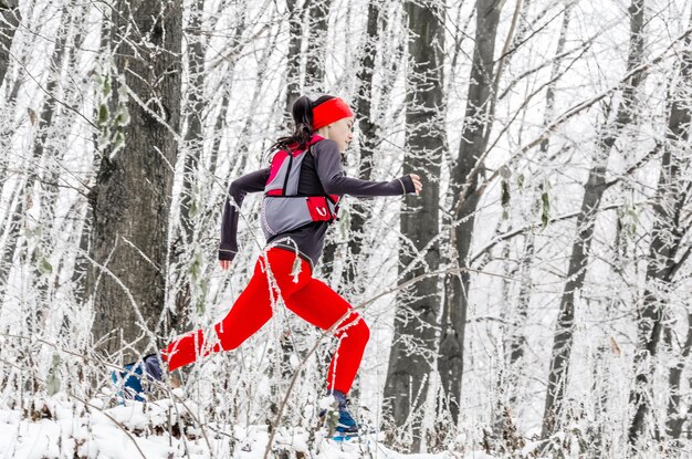 Jonge vrouw atleet in rode legging loopt in het bos van de winter zijaanzicht wintersport extreme