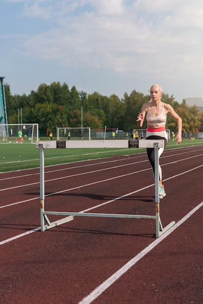 Jonge vrouw atleet loper die hindernissen in het stadion buiten loopt