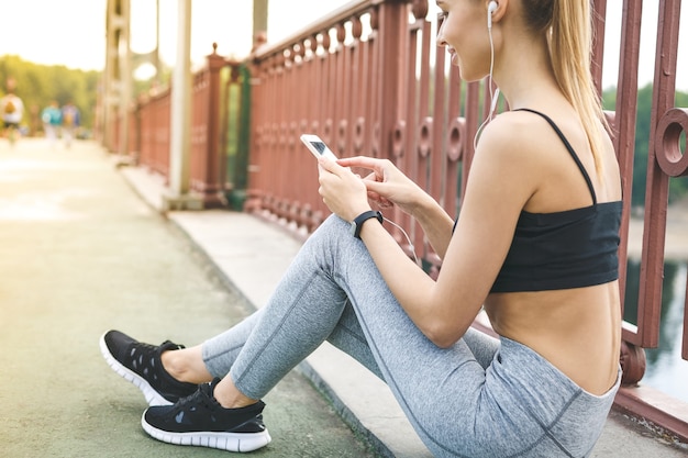 Jonge vrouw atleet zittend op straat met mobiele telefoon