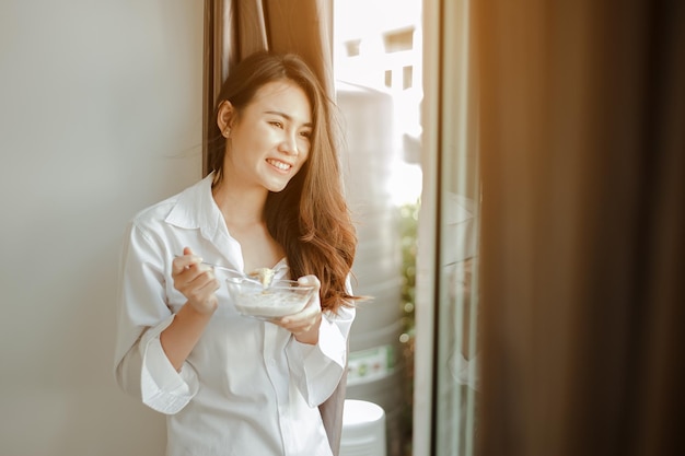 Jonge vrouw azië wordt 's ochtends verfrist wakker en eet koffie, cornflakes, brood en appel als ontbijt thuis op vakantie. Aziatisch, Azië, ontspannen, ontbijt, vernieuwen, lifestyle concept.