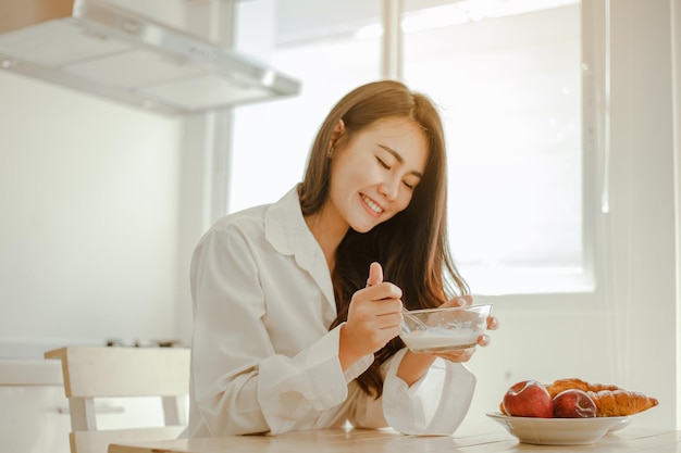 Jonge vrouw azië wordt 's ochtends verfrist wakker en eet koffie, cornflakes, brood en appel als ontbijt thuis op vakantie. Aziatisch, Azië, ontspannen, ontbijt, vernieuwen, lifestyle concept.