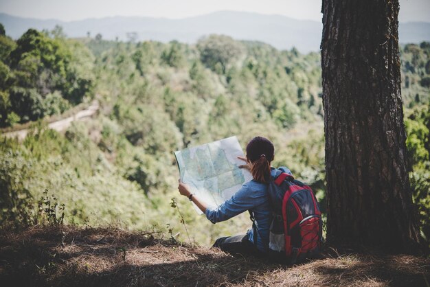 Foto jonge vrouw, backpacker, wandelaar, kaart lezen, wandeling, wegkijken om een plek te vinden om te gaan, avontuurlijke vakantie.