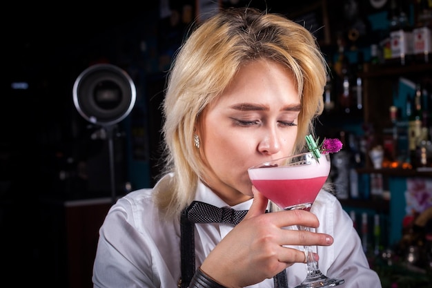 Jonge vrouw bartending maakt een cocktail terwijl ze bij de toog in de bar staat