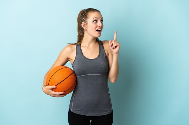 Jonge vrouw basketbal geïsoleerd op blauw denken een idee met de vinger omhoog