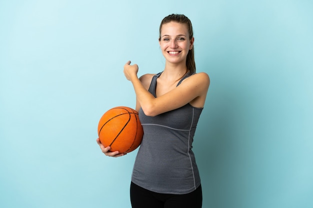 Jonge vrouw basketbal geïsoleerd op blauw terug te wijzen