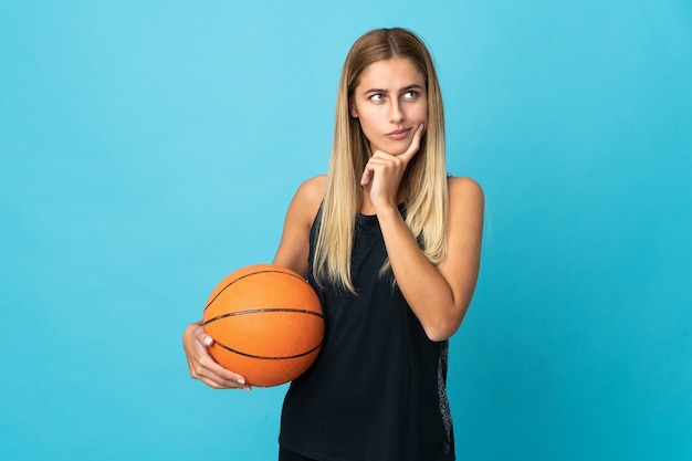 Jonge vrouw basketbal spelen geïsoleerd op een witte muur twijfels en denken