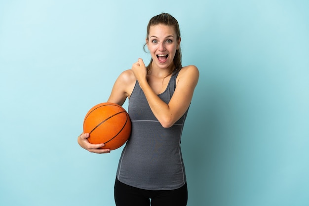 Jonge vrouw basketbal spelen op blauw een overwinning vieren