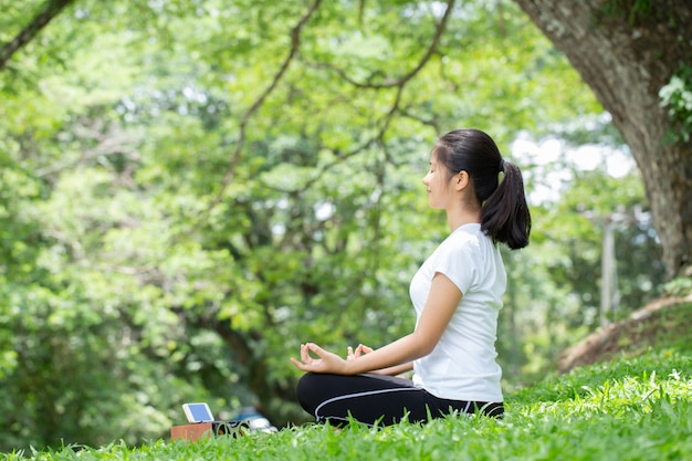 Jonge vrouw beoefenen van yoga en luisteren naar muziek in de natuur. Aziatische vrouw beoefent yoga in stadspark