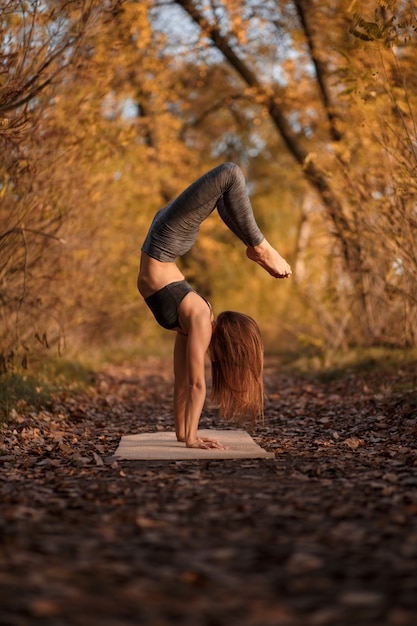 Jonge vrouw beoefenen van yoga oefening in herfst park met gele bladeren.