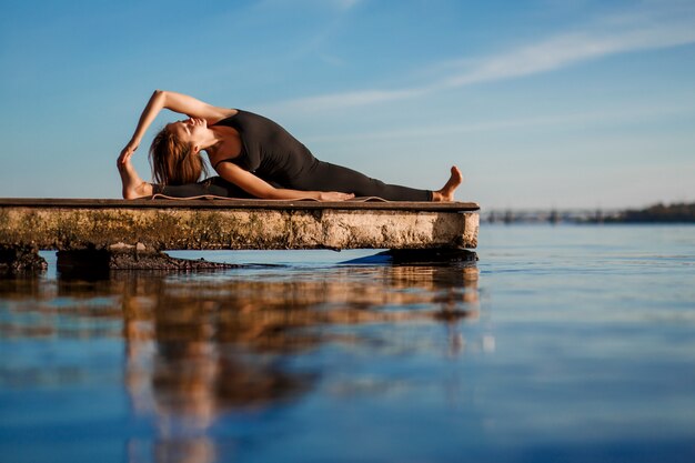 Foto jonge vrouw beoefenen van yoga oefening op rustige houten pier