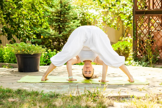 Jonge vrouw beoefent yoga in de tuin prasarita padottanasana of wide stance forward bend