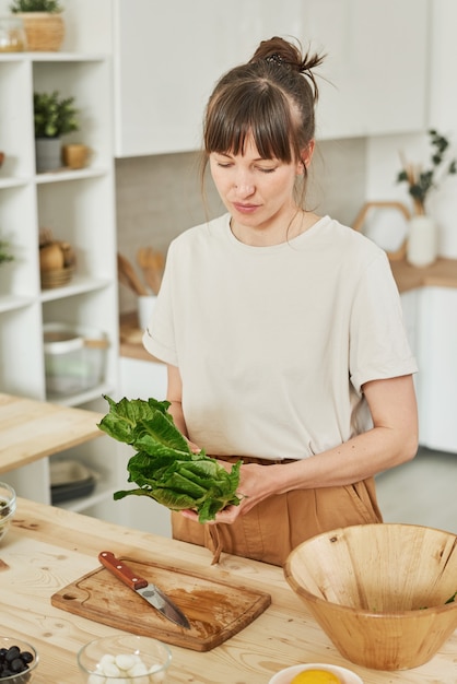 Jonge vrouw bereidt groentesalade voor het avondeten terwijl ze in de keuken staat