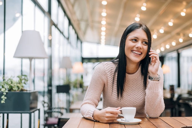 Jonge vrouw bij koffie drinken koffie en praten op de mobiele telefoon.