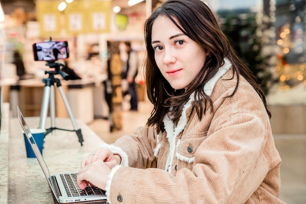 Jonge vrouw blogger in het winkelcentrum die aan een laptop werkt