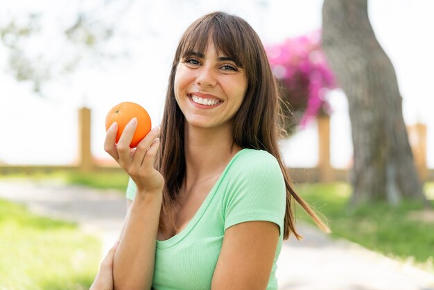 Jonge vrouw buiten met een sinaasappel met een gelukkige uitdrukking