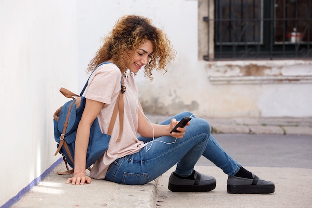 Jonge vrouw buiten zitten met mobiele telefoon en oortelefoons