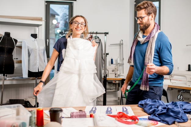 Jonge vrouw cliënt die trouwjurk past met man kleermaker staande in de naaistudio
