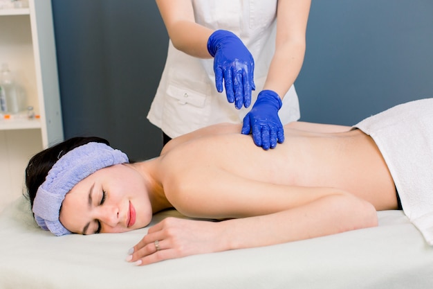 Jonge vrouw cosmetologist rugmassage doen in spa salon voor jonge mooi meisje