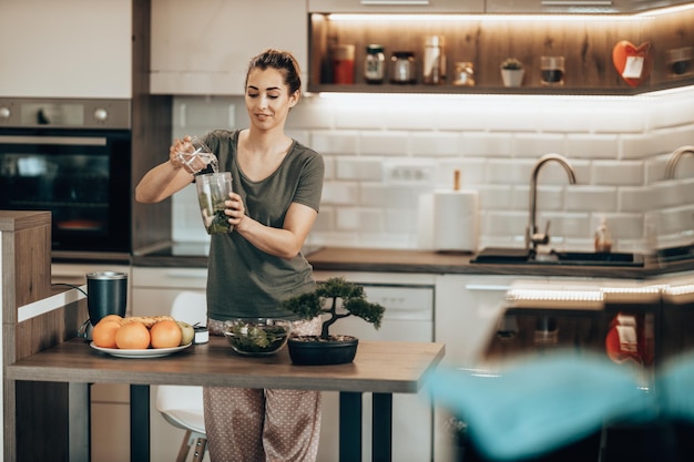 Jonge vrouw dagdromen terwijl ze van de ochtend geniet en thuis een smoothie bereidt.