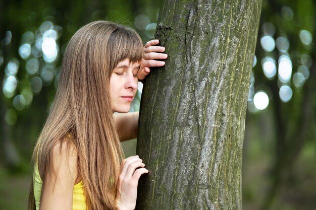 Foto jonge vrouw die aan boomstam in de zomerbos leunt