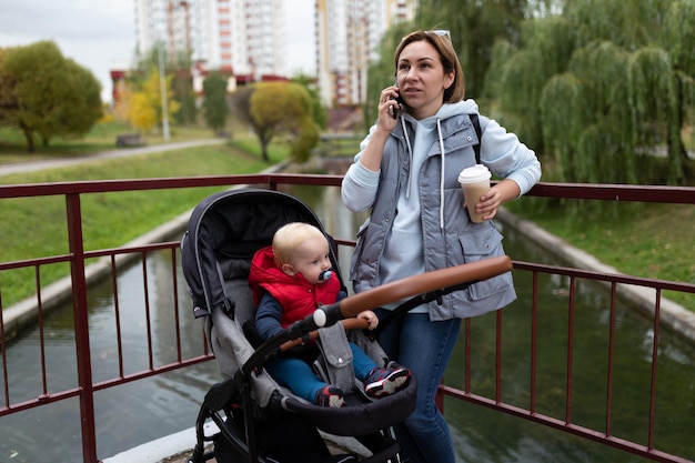 Jonge vrouw die aan de telefoon praat terwijl ze naast de kinderwagen loopt waarin de baby zit