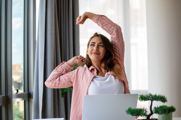 Jonge vrouw die aan een laptop werkt Zakelijke vrouw die bezig is met het werken aan een laptop Stretching Zakelijke vrouw zit aan een helder modern werkstation