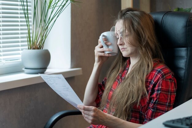 Jonge vrouw die aan hoofdpijn lijdt op het werk. secretaresse in leren stoel leest documenten, leunend tegen het hoofd.