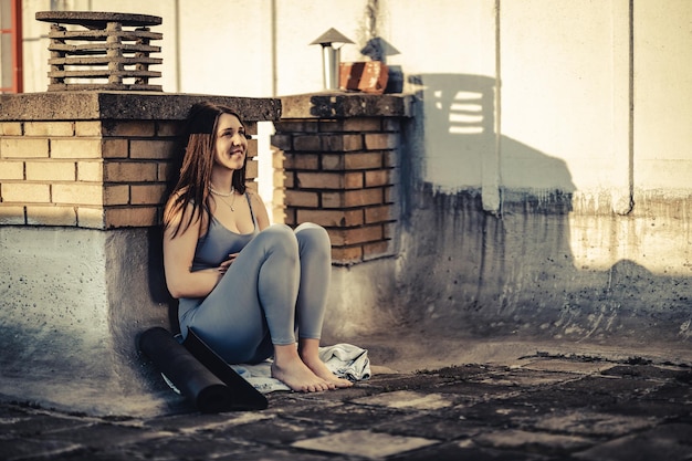 Jonge vrouw die aan iets denkt terwijl ze zich voorbereidt op een yogatraining op een dakterras bij zonsondergang.