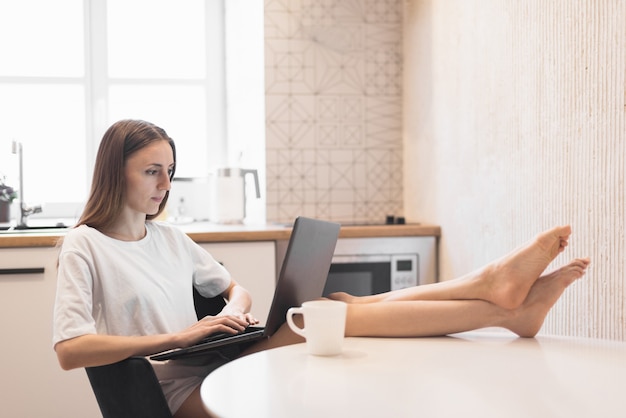 Jonge vrouw die aan laptop bij keuken werkt. Vrouwelijke freelancer die thuis online werkt. Selectieve focus