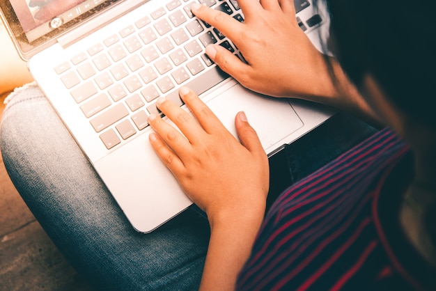 Jonge vrouw die aan laptop computer werkt terwijl het zitten op de vloer