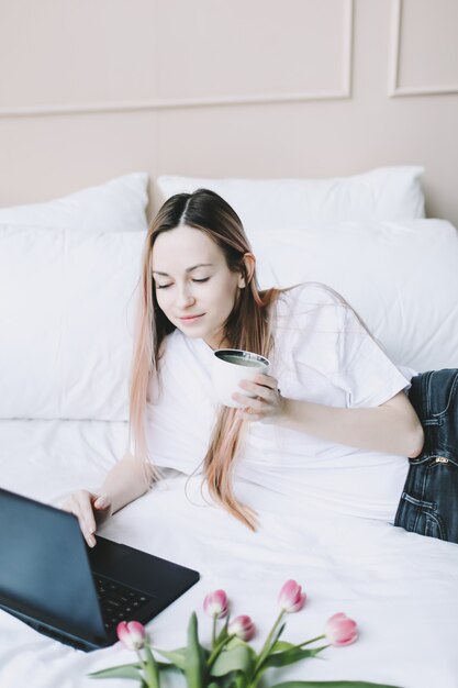 Jonge vrouw die aan laptop in bed thuis werkt