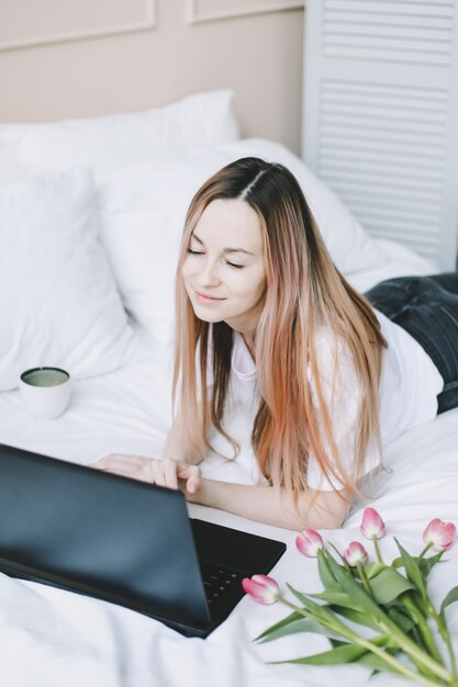 Jonge vrouw die aan laptop in bed werkt