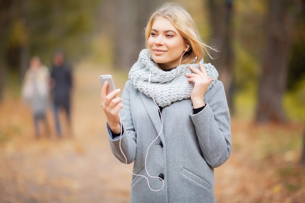 Jonge vrouw die aan muziek in de herfstbos luistert