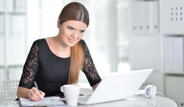 Jonge vrouw die aantekeningen maakt en laptop gebruikt