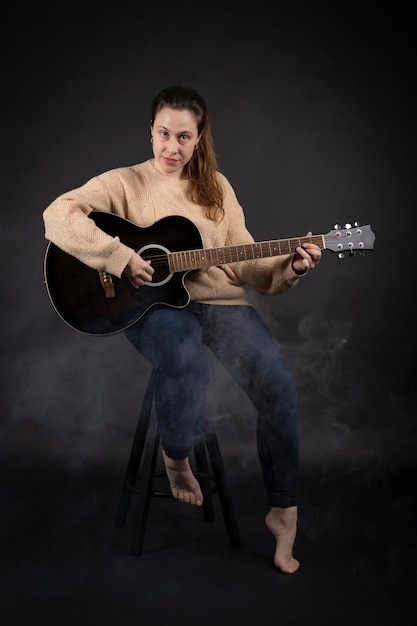 Jonge vrouw die akoestische gitaar speelt met rook en zwarte achtergrond