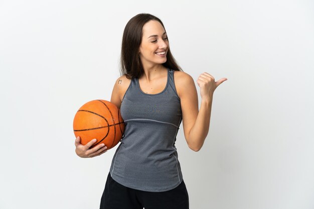 Jonge vrouw die basketbal speelt over een geïsoleerde witte achtergrond die naar de zijkant wijst om een product te presenteren