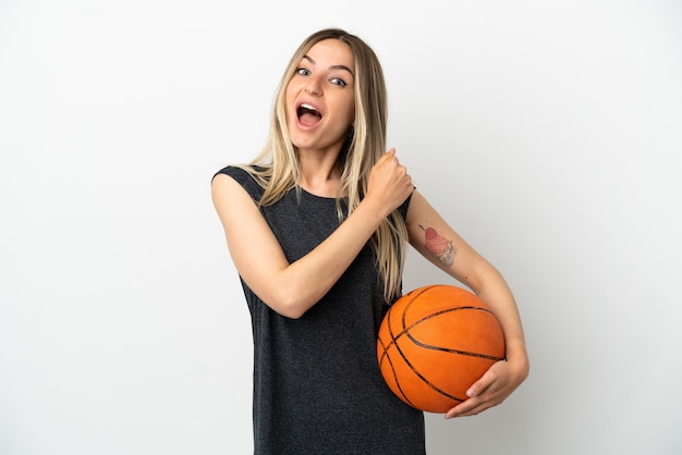 Jonge vrouw die basketbal speelt over geïsoleerde witte muur die een overwinning viert