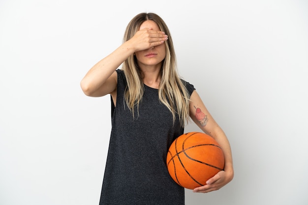 Jonge vrouw die basketbal speelt over geïsoleerde witte muur die ogen behandelt door handen. Wil je iets niet zien