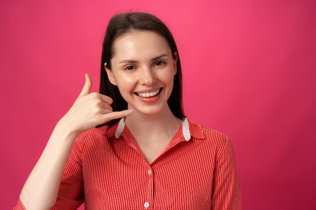 Jonge vrouw die bel me teken toont tegen roze achtergrond