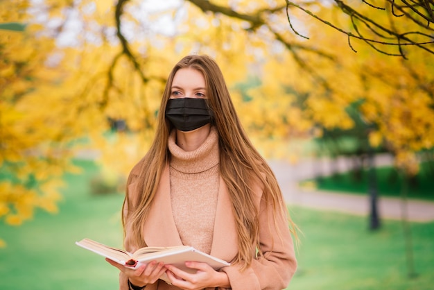 Jonge vrouw die beschermt tegen het coronavirus tijdens het wandelen in het park. Herfst achtergrond.