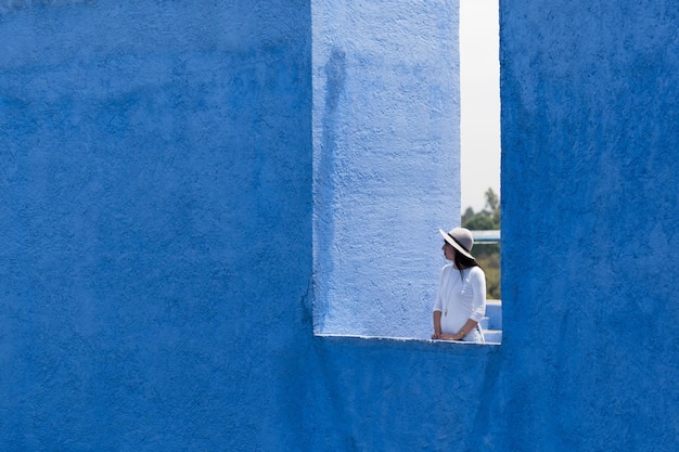 Jonge vrouw die bij de blauwe muur staat.
